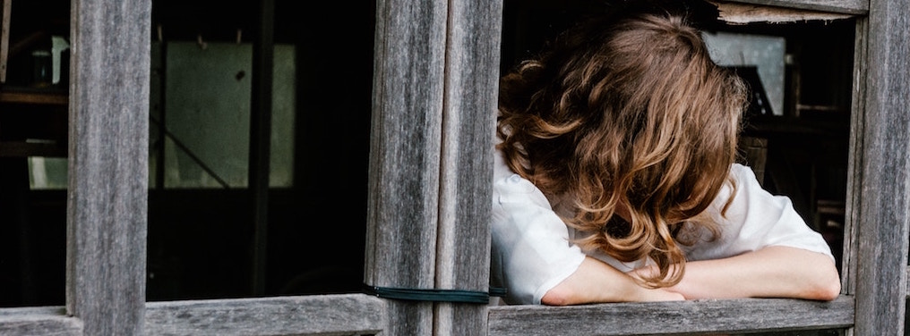 Femme dont on ne voit pas le visage les bras sur le bord d'une fenêtre