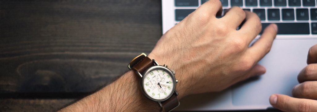 Homme qui travaille sur un portable et regarde sa montre analogue