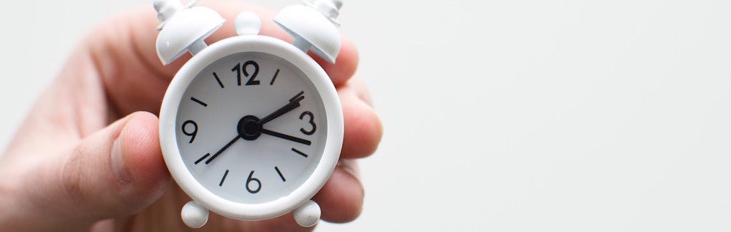 Main d'un homme qui tient un petit réveil matin blanc