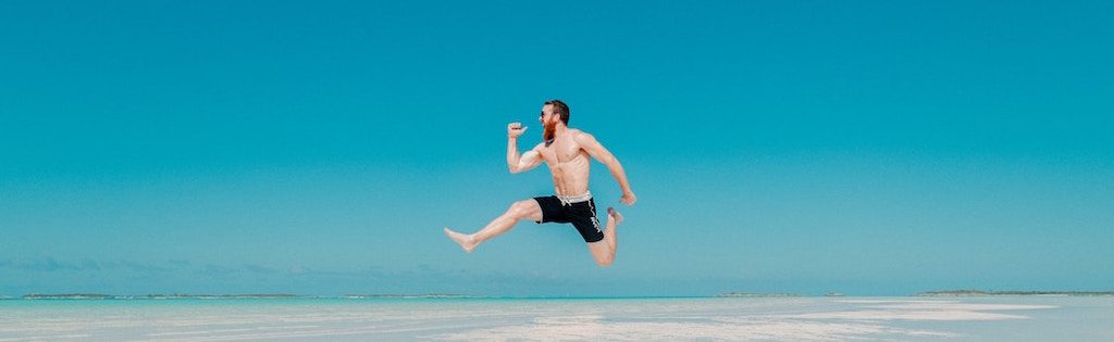 Homme qui saute de joie sur la plage devant un ciel azur