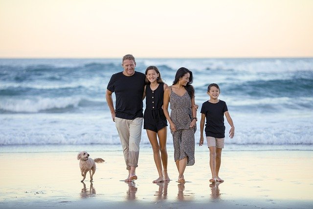Famille de 4 avec chien devant la mer, les pieds sur le sable humide